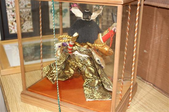 A Japanese wooden cased model of a Samurai warrior holding aloft a fan, with ornate silkwork robes, overall height 35cm, width 33cm